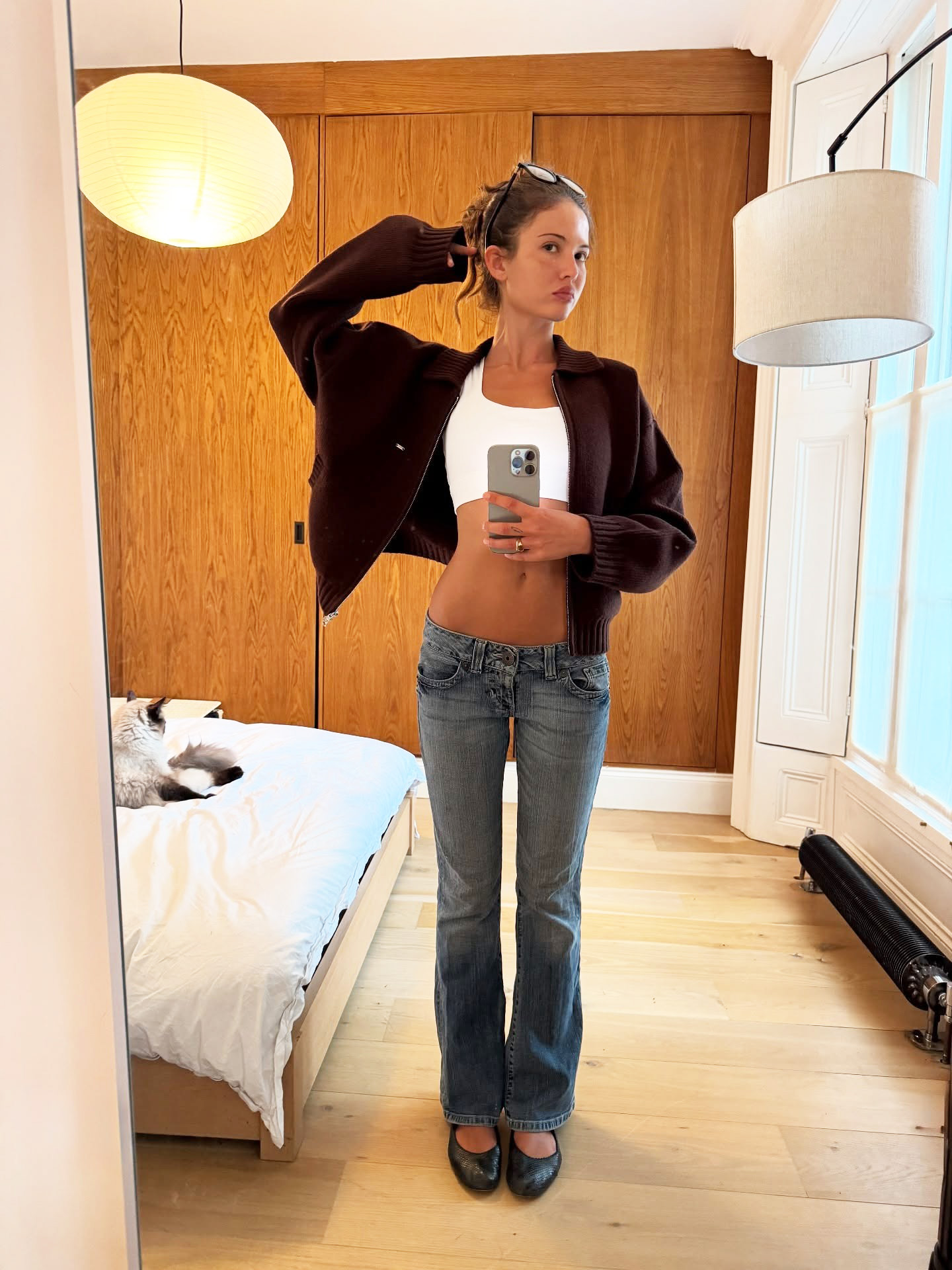 A woman wearing a brown knit sweater, white tank top, and blue bootcut jeans and black flats