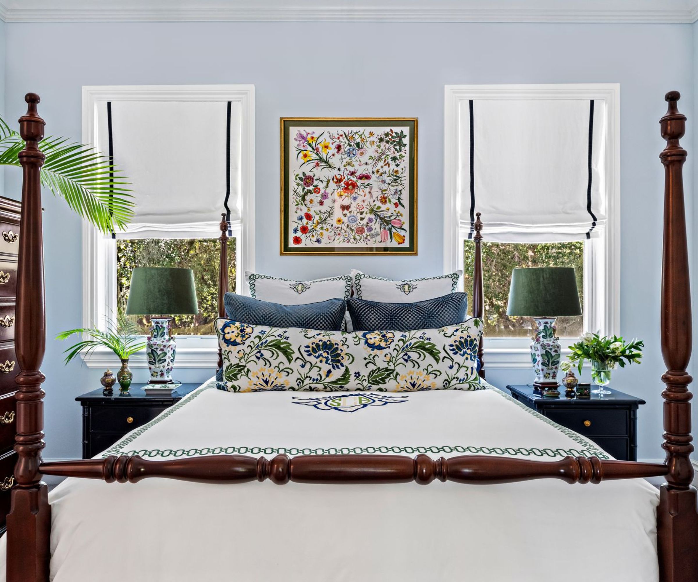 Bedroom with pale blue walls, dark four-posted wood bed, embroidered bedding and two bedside tables with blue and white antique lamps