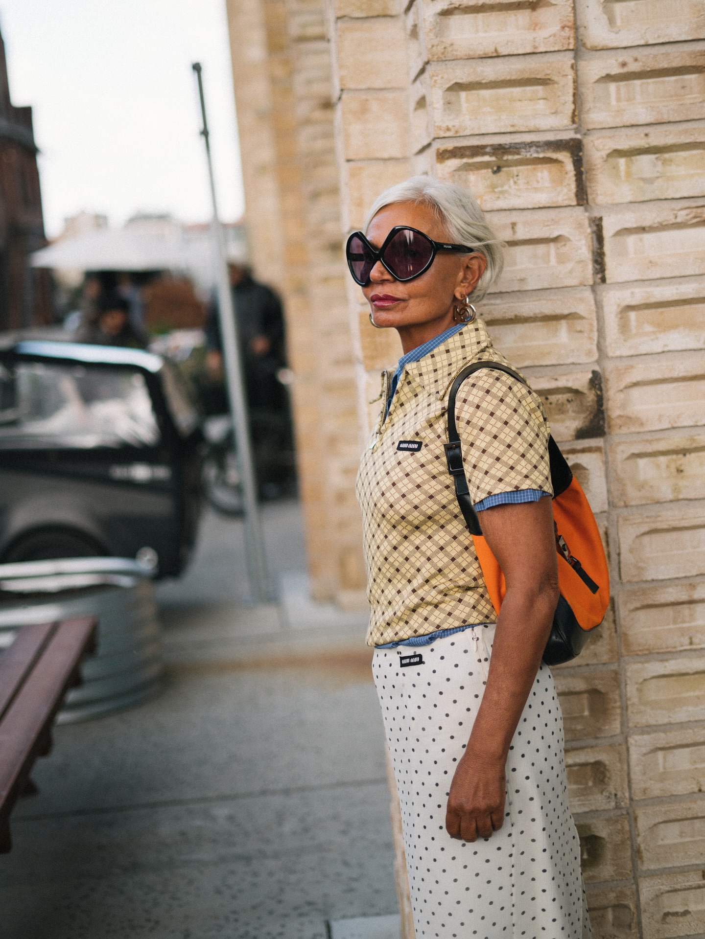 An image of @greceghanem wearing an orange bag with a polka dot skirt and a check top.
