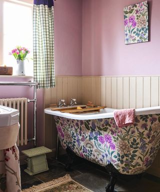 A bathroom with pink walls, floral wall art and bathtub decorated with floral design