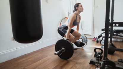 Woman working out while on lockdown. She is lifting a barbell with weights in her home gym, crouching