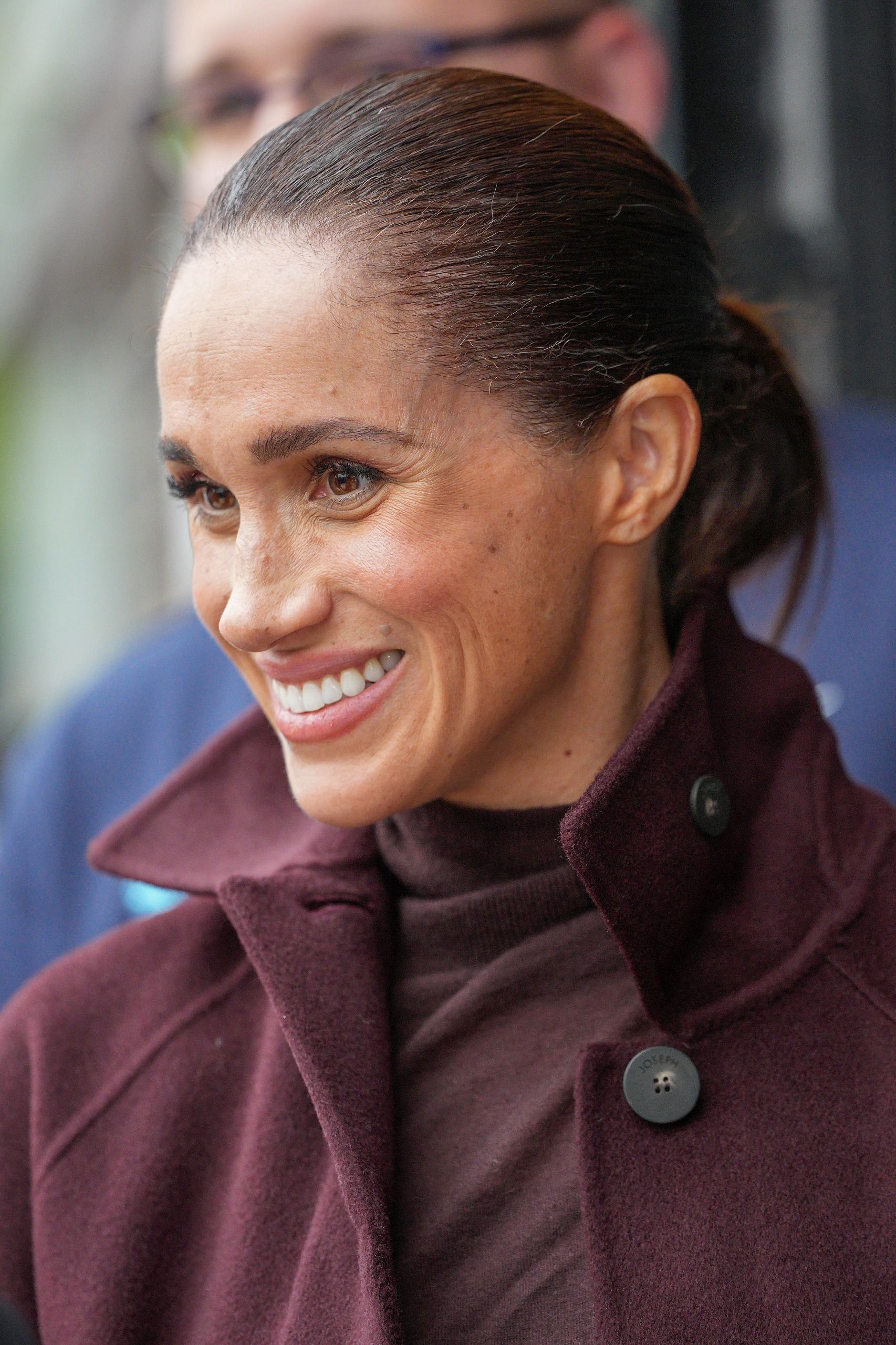 Meghan Markle wearing a maroon coat and smiling