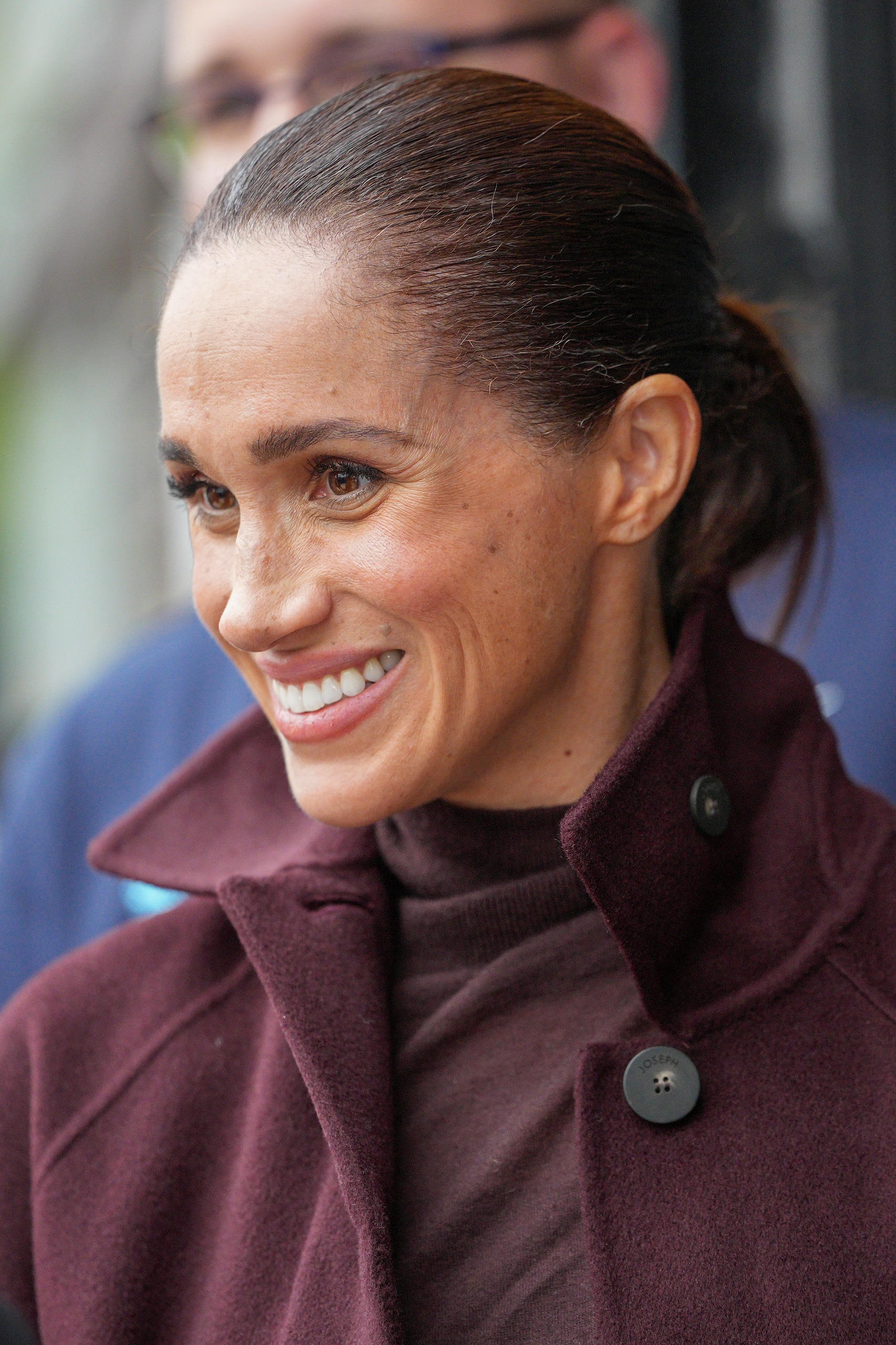 Meghan Markle wearing a maroon coat and smiling