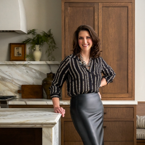 Image of a woman in a striped blouse and black leather skirt standing in a marble and wood kitchen