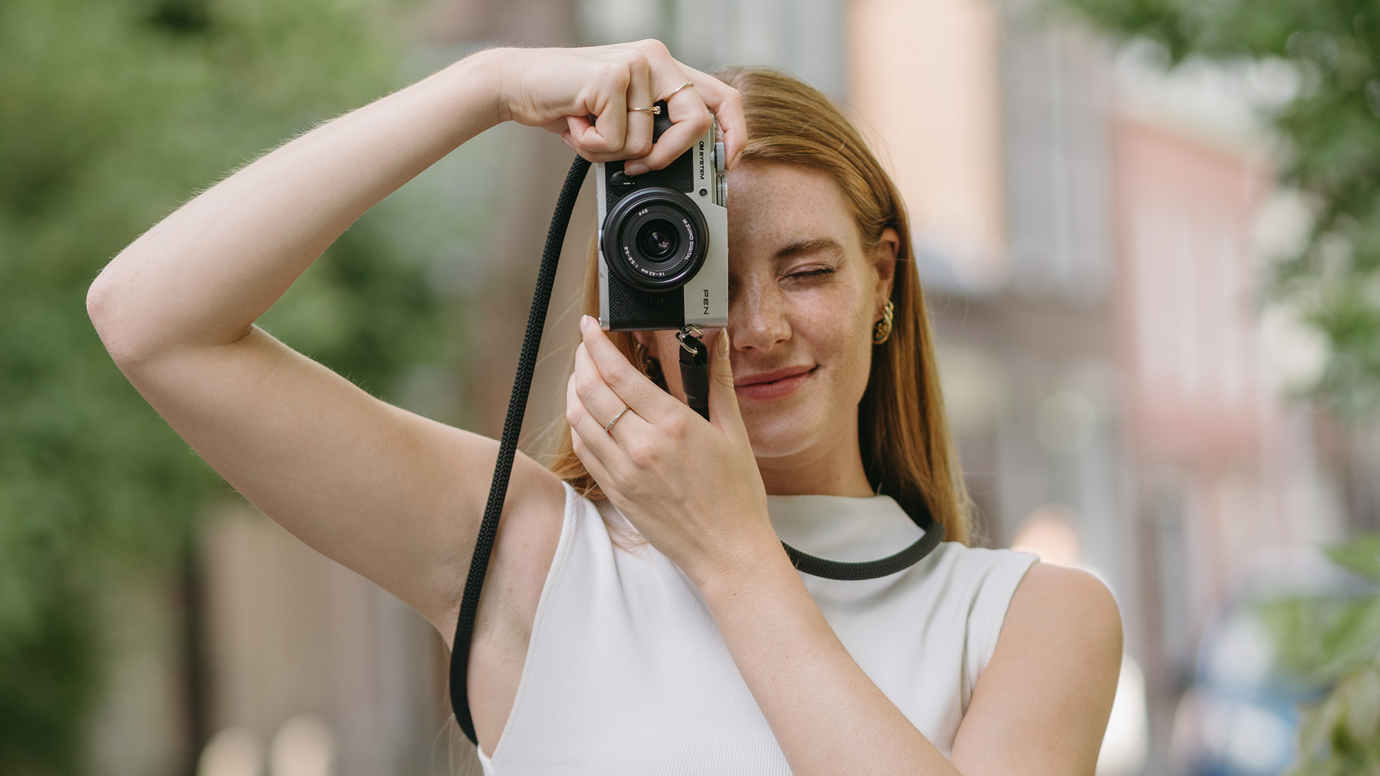 OM System PEN lifestyle image of person holding camera and looking through viewfinder 