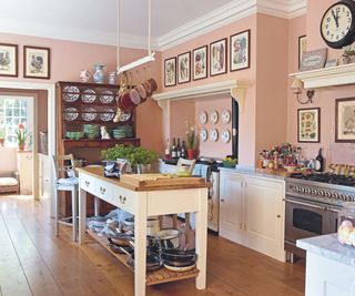 Pink walls, hanging pots, white kitchen island wooden countertop