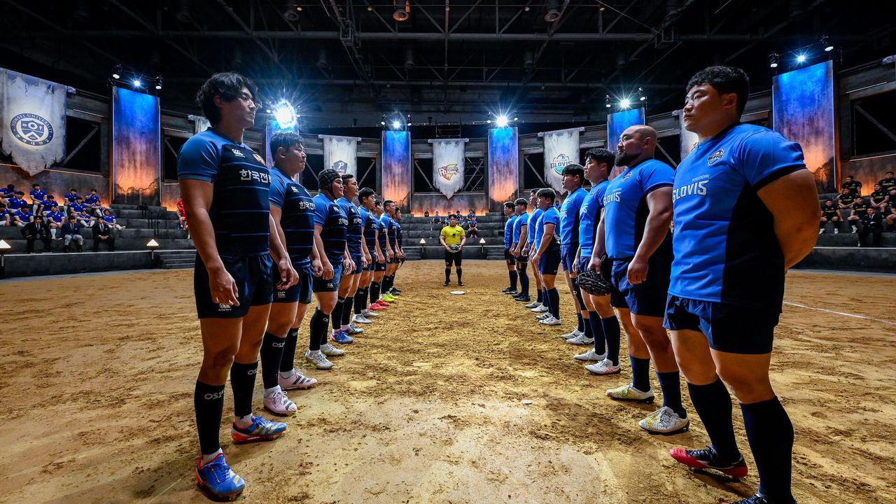 Two teams line up to face off in a circular dirt arena, with a referee in yellow at the center, in Netflix&#039;s &#039;Rugged Rugby: Conquer or Die.&#039;