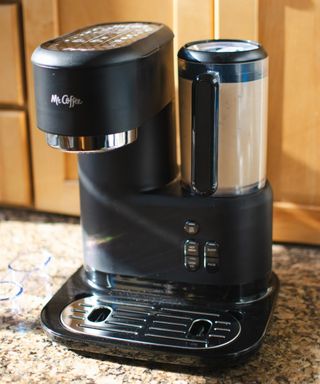 Front-on view of the Mr. Coffee® Single-Serve Frappe™, Iced, and Hot Coffee Maker blender on granite kitchen worktop with light wood cabinetry in background