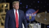 President Donald Trump in a red tie surrounded by NASA hardware