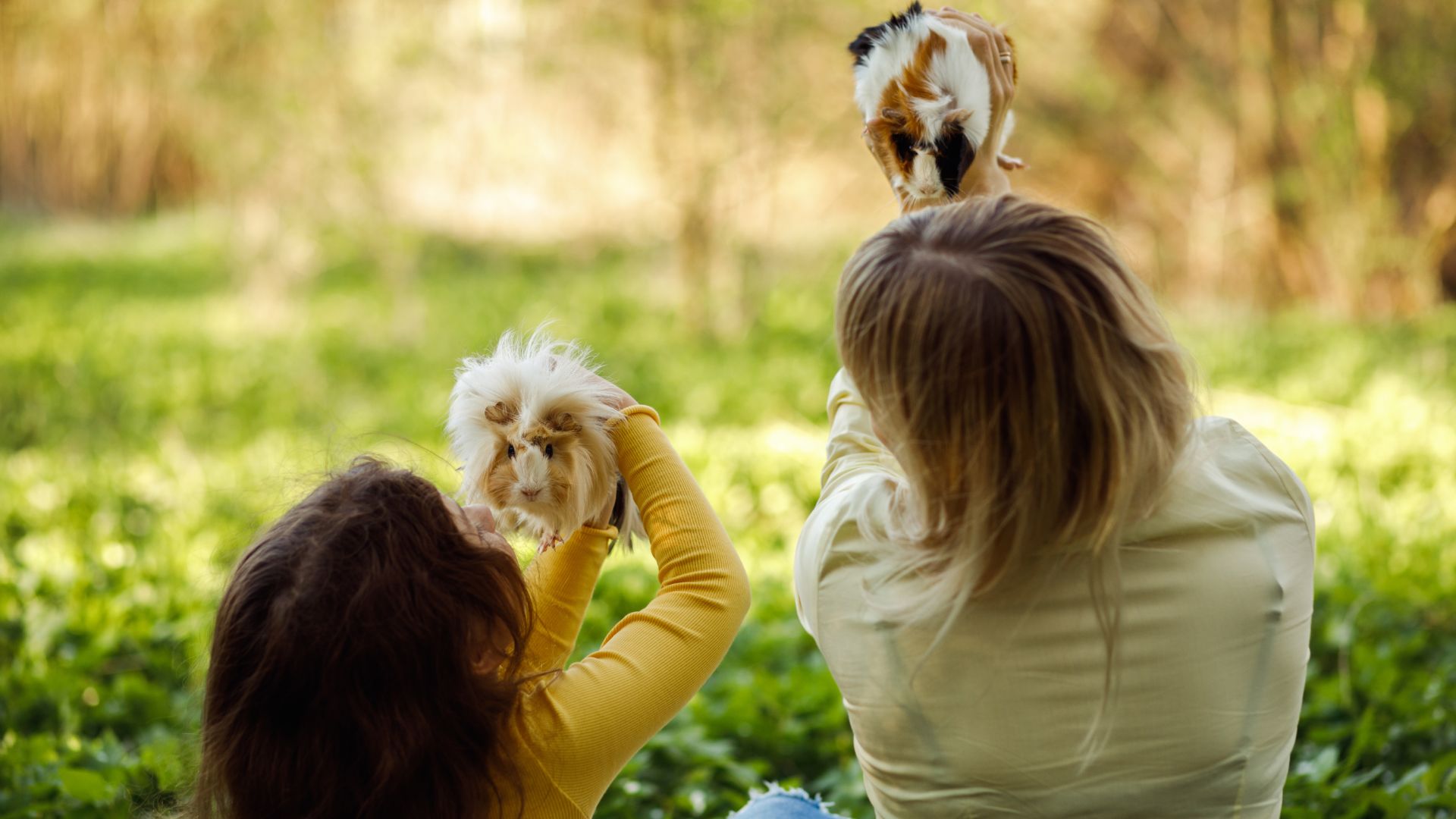 A child and woman holding up two guinea pigs