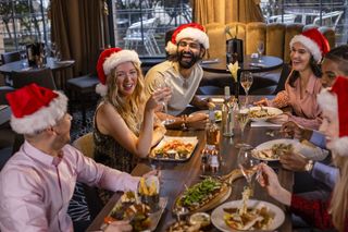 A group of happy people wearing Santa hats, enjoying a festive meal out.
