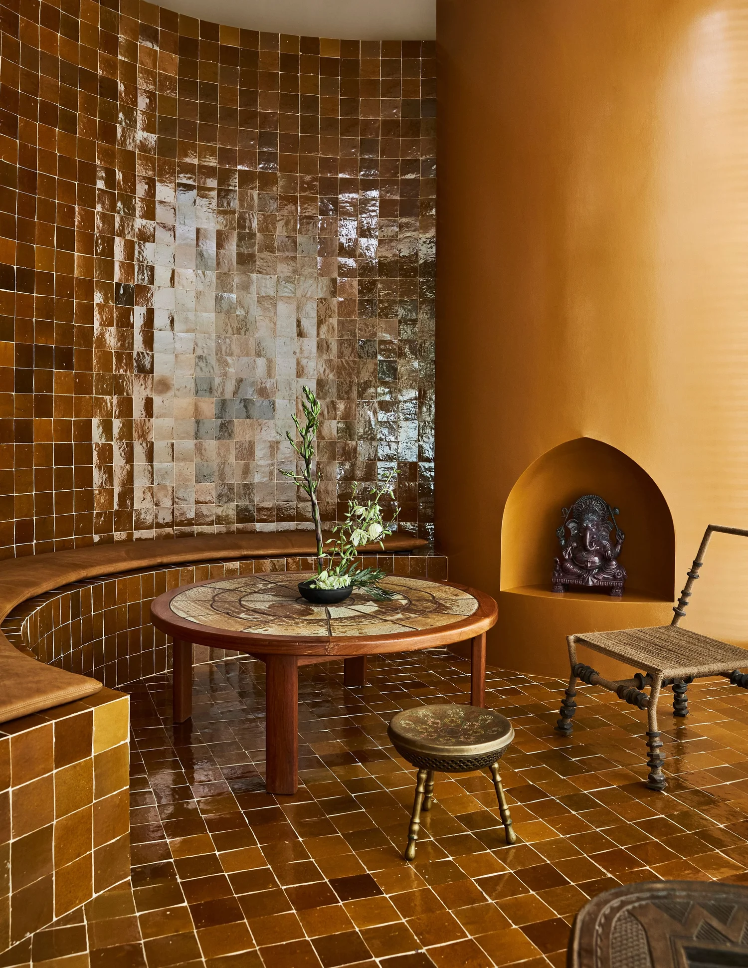 Image of a sitting room/dining nook that is drenched in caramel brown tiles and has a curved built-in bench seat. There is a circular fireplace that is painted in a matching color.