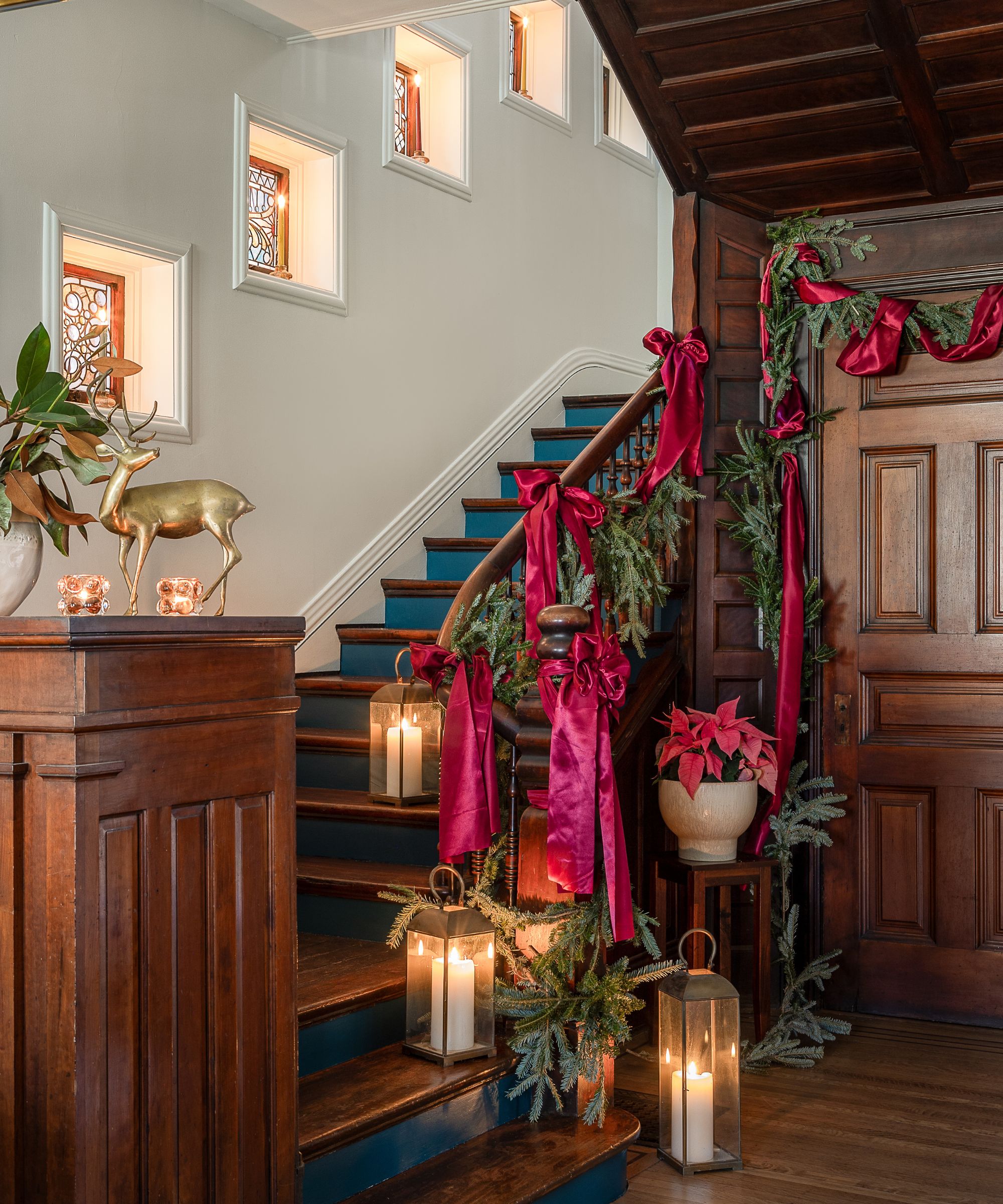 dark wooden entryway with historic dark wooden stairs decorated for christmas with garlands, satin bows, and lanterns
