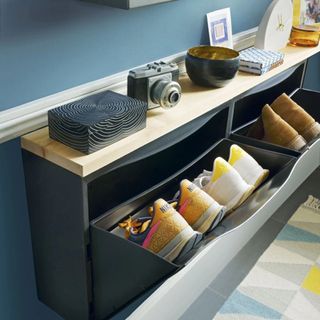 storage cabinet and shoe rack containing trainers with a camera, bowl and clock on the wooden countertop