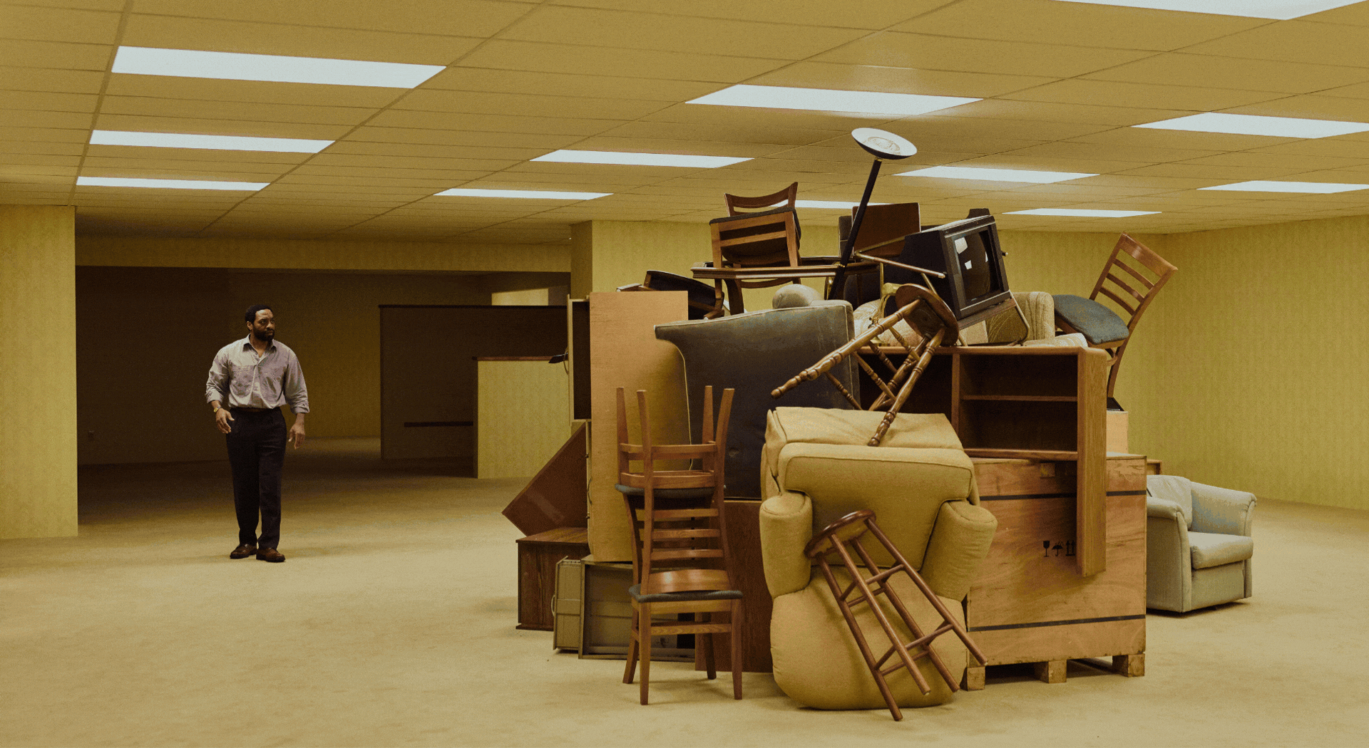 Rotating gif showcasing a pale yellow-painted, office-like environment inhabited by nothing but a handful of objects, with people wandering through it.