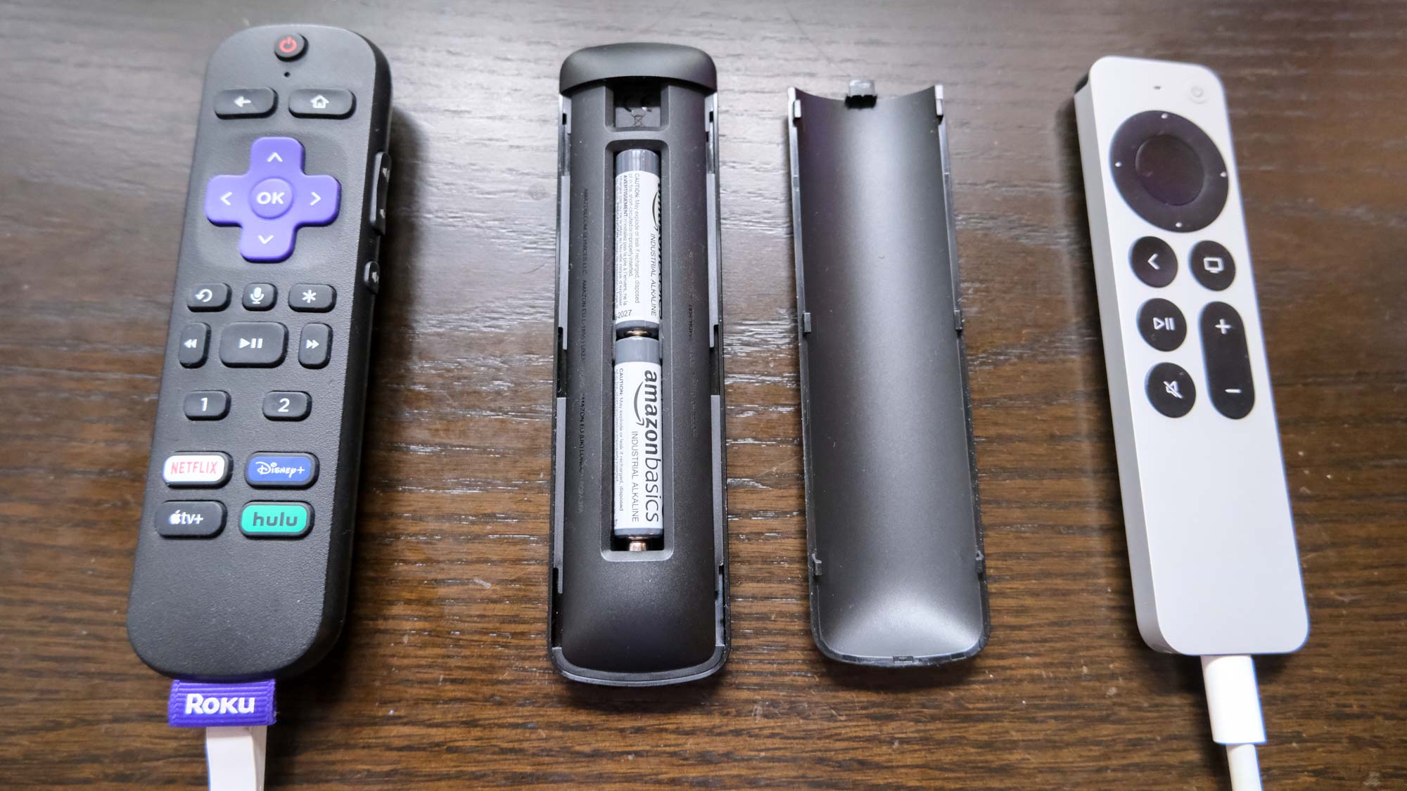 (L to R) the Roku Voice Remote Pro charging with USB cable, The Alexa Voice Remote Pro (from behind) and the Apple TV Siri remote charging