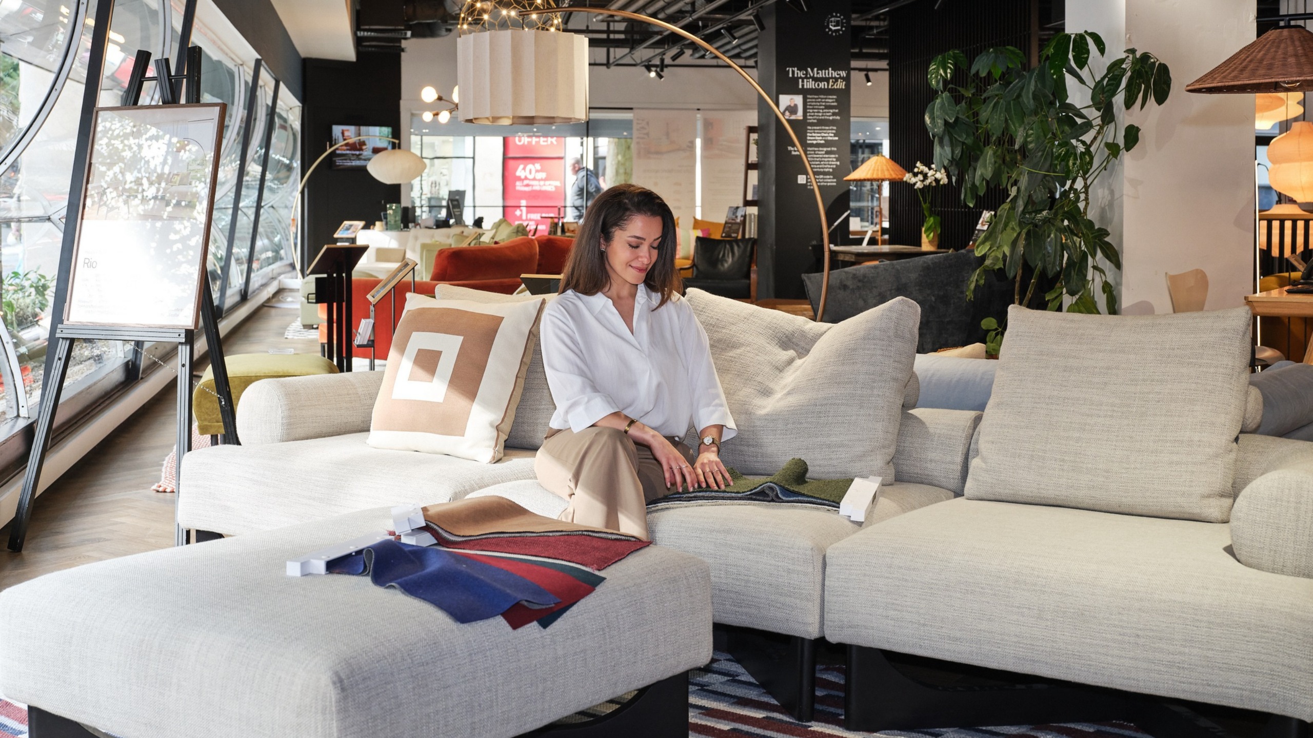 Interior stylist Miaad Latoof testing the Heal&rsquo;s Rio 4 Seater Sofa in the Heal&rsquo;s flagship showroom, with upholstery swatches laid across the sofa.