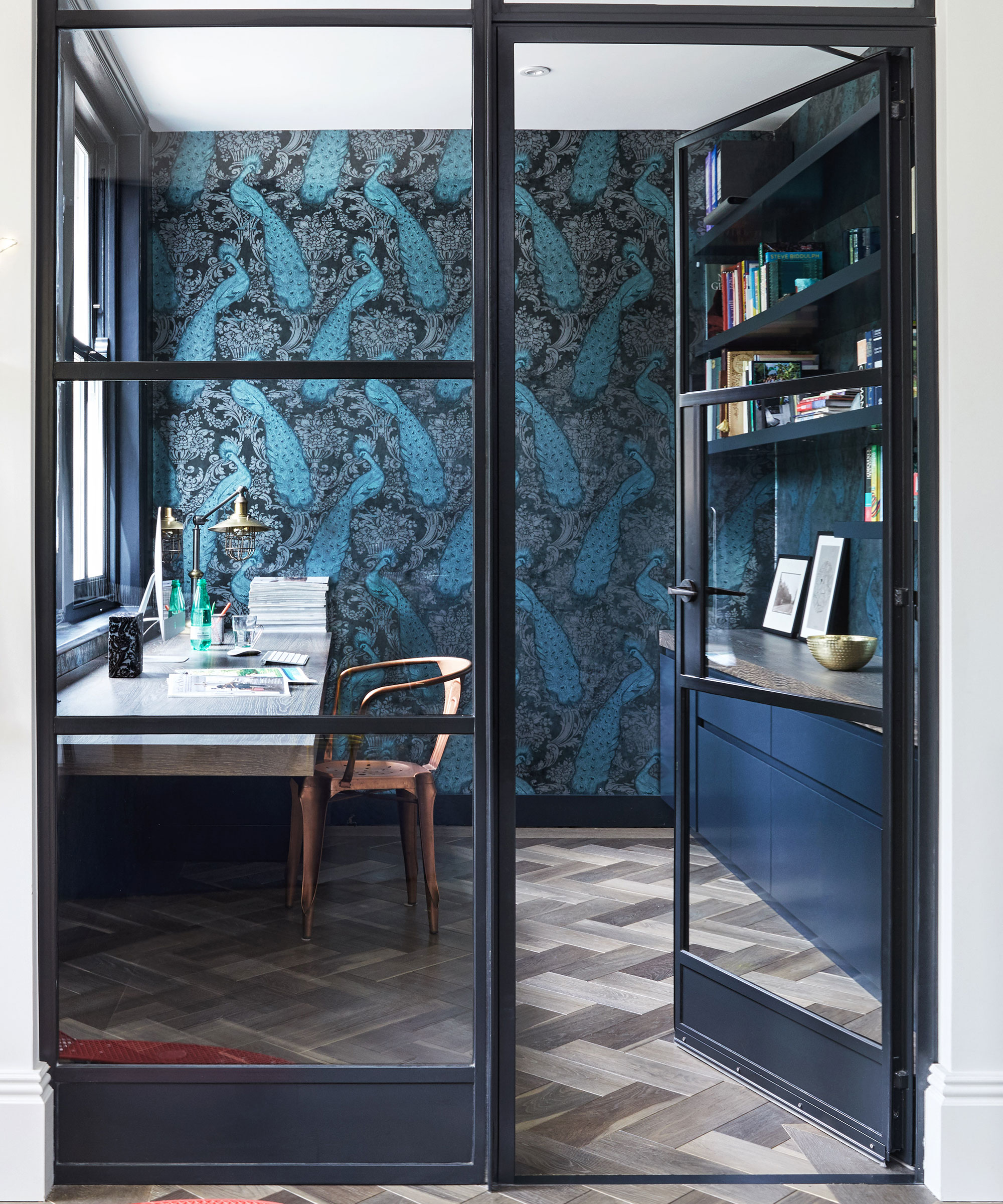 An example of a home office box room idea with dark blue walls, glass door and built-in shelving