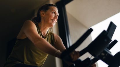 Woman doing 10-minute cycling workout on bike at home, smiling