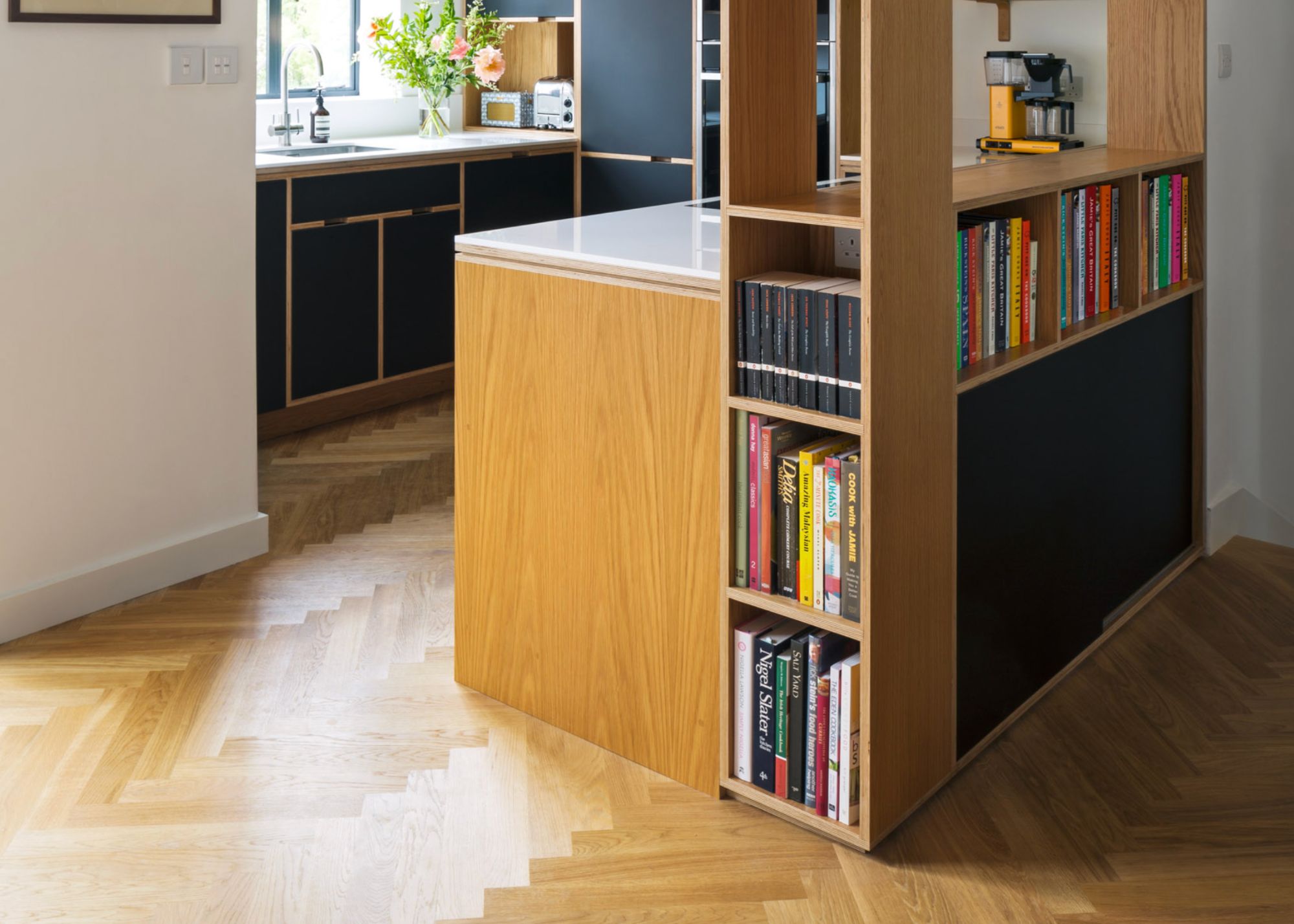 A small kitchen with wooden plank flooring, and a divider with books in them