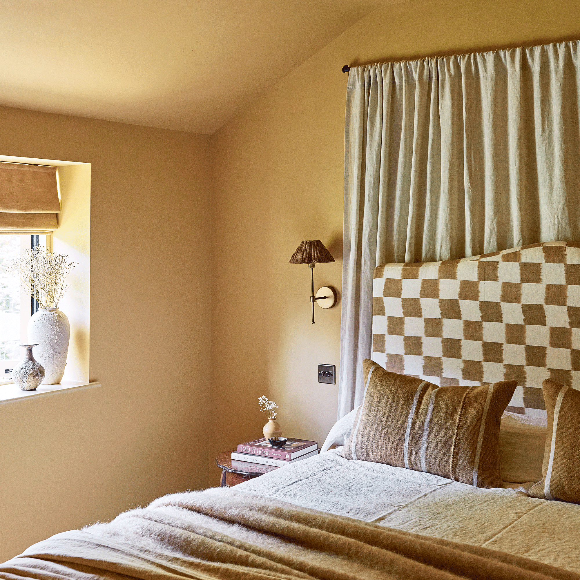 a bedroom with yellow walls, a checkered print headboard and a wall-hung curtain behind it