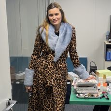 French style editor and write Eugenie Trochu poses in the Vogue France offices with a chic designer outfits ideas featuring a leopard-print coat with a blue fur collar