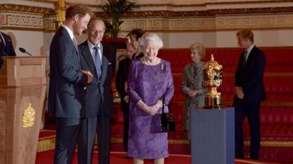 Prince Harry, Prince Philip, Duke of Edinburgh and Queen Elizabeth II look at the Webb Ellis Cup on a plinth during a Rugby World Cup reception at Buckingham Palace on October 12, 2015 in London.