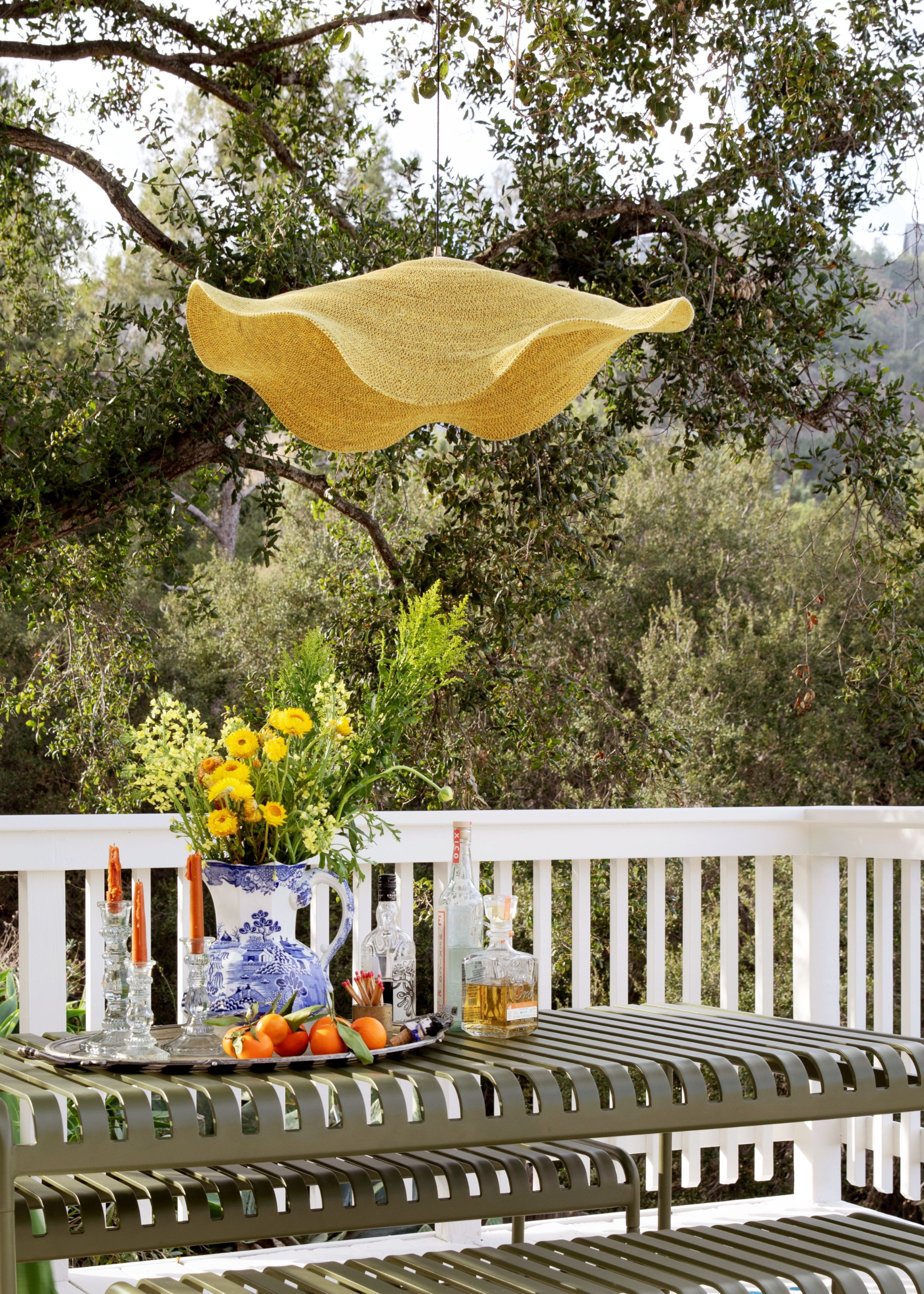 Pooky x The Novogratz pendant light hanging overhead a sage green aluminum dining table and bench set up.