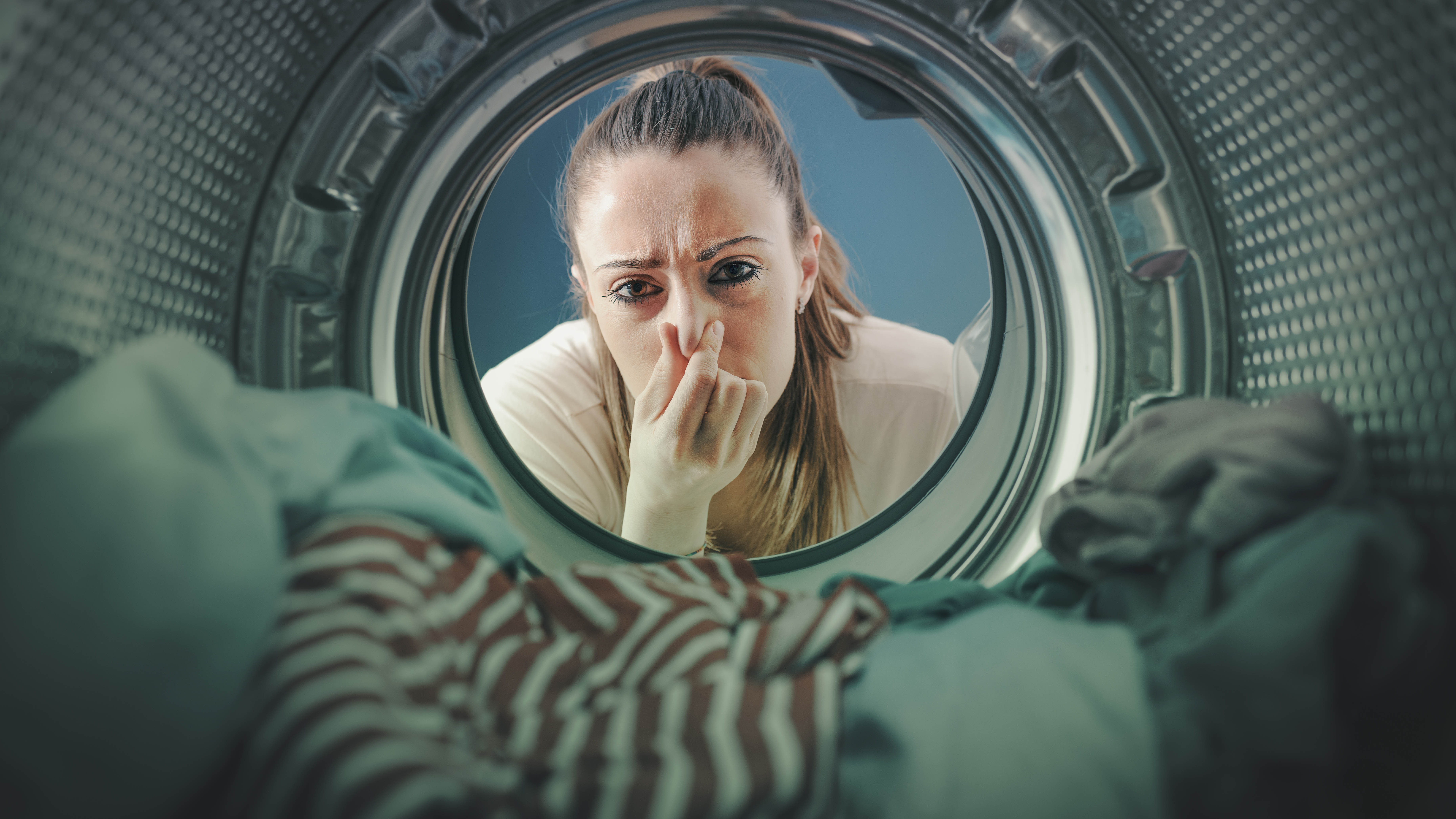 A woman holding her nose as she looks at laundry inside the washing machine