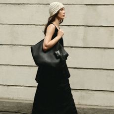Lena wears a black maxi dress, crochet hat, and black tote bag.