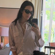 Alexa Chung takes a mirror selfie wearing white frayed jeans with an oversized shirt and t-shirt.