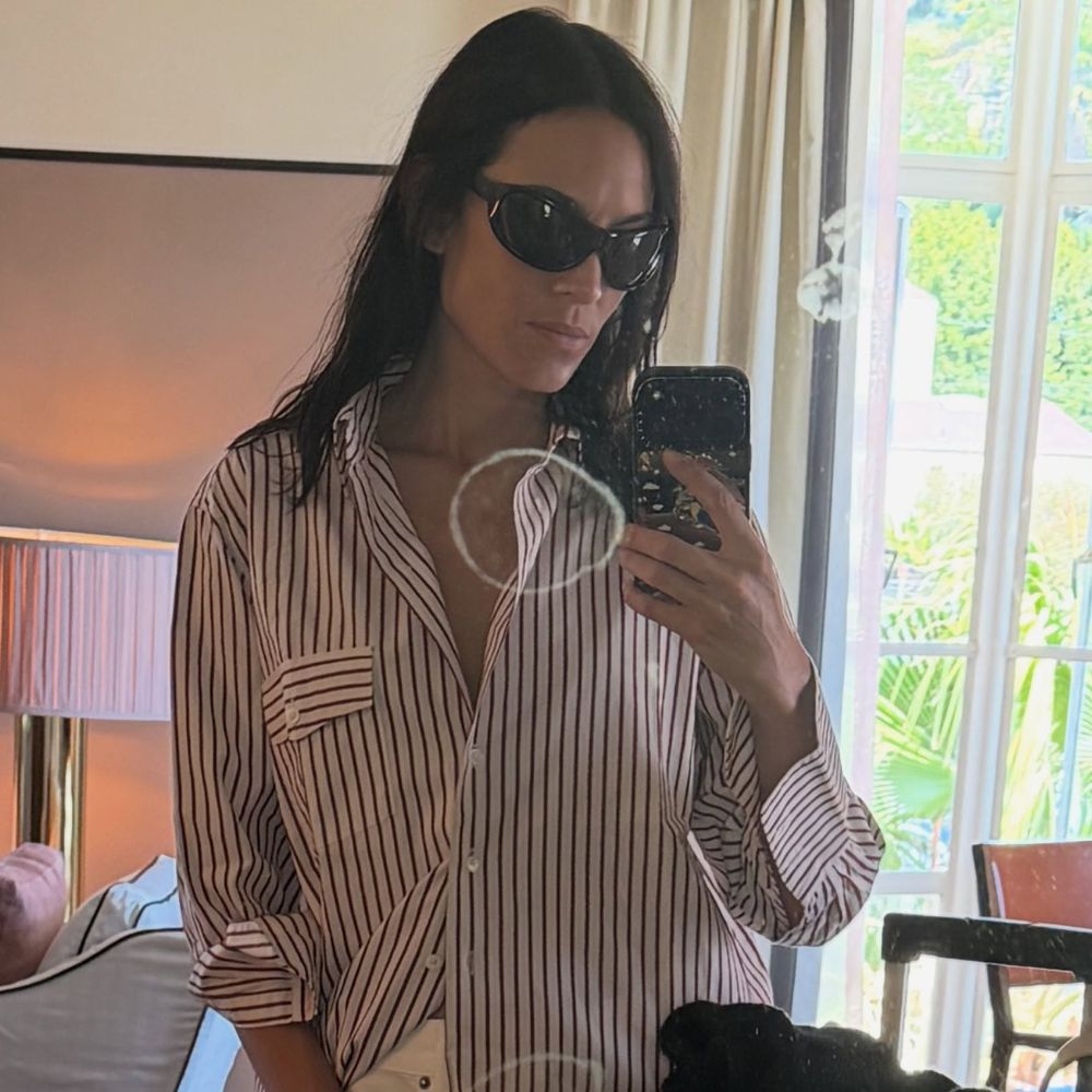 Alexa Chung takes a mirror selfie wearing white frayed jeans with an oversized shirt and t-shirt.