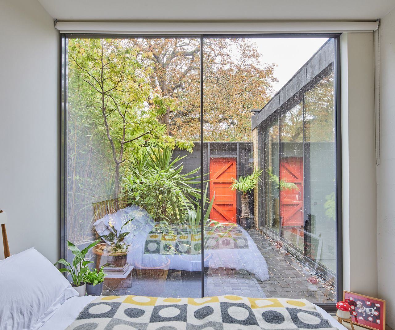 A ground floor bedroom with sliding glass doors spanning the floor to the ceiling across the length of one wall. The view out is to a small private courtyard with lush greenery