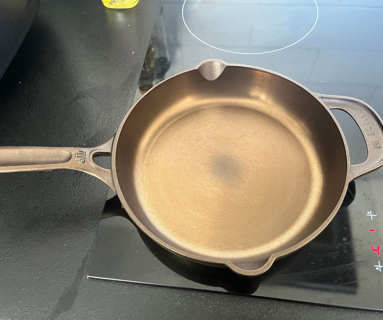A small bronze colored cast-iron skillet on a black glass stove.