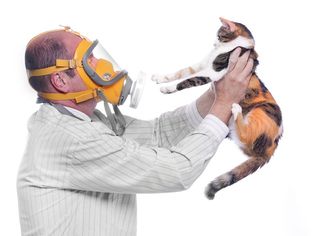 A man wearing a gas mask holds a cat at an arm's length