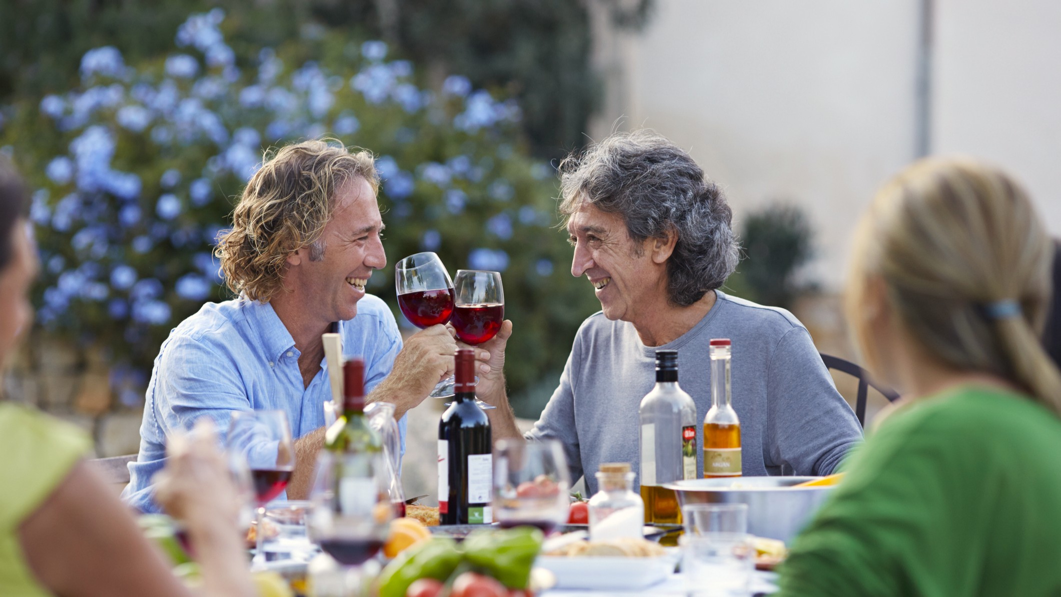 Two older men toast at a Spanish outdoor dinner party or lunch.