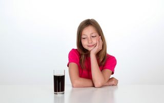 A girl looks at a glass full of cola.