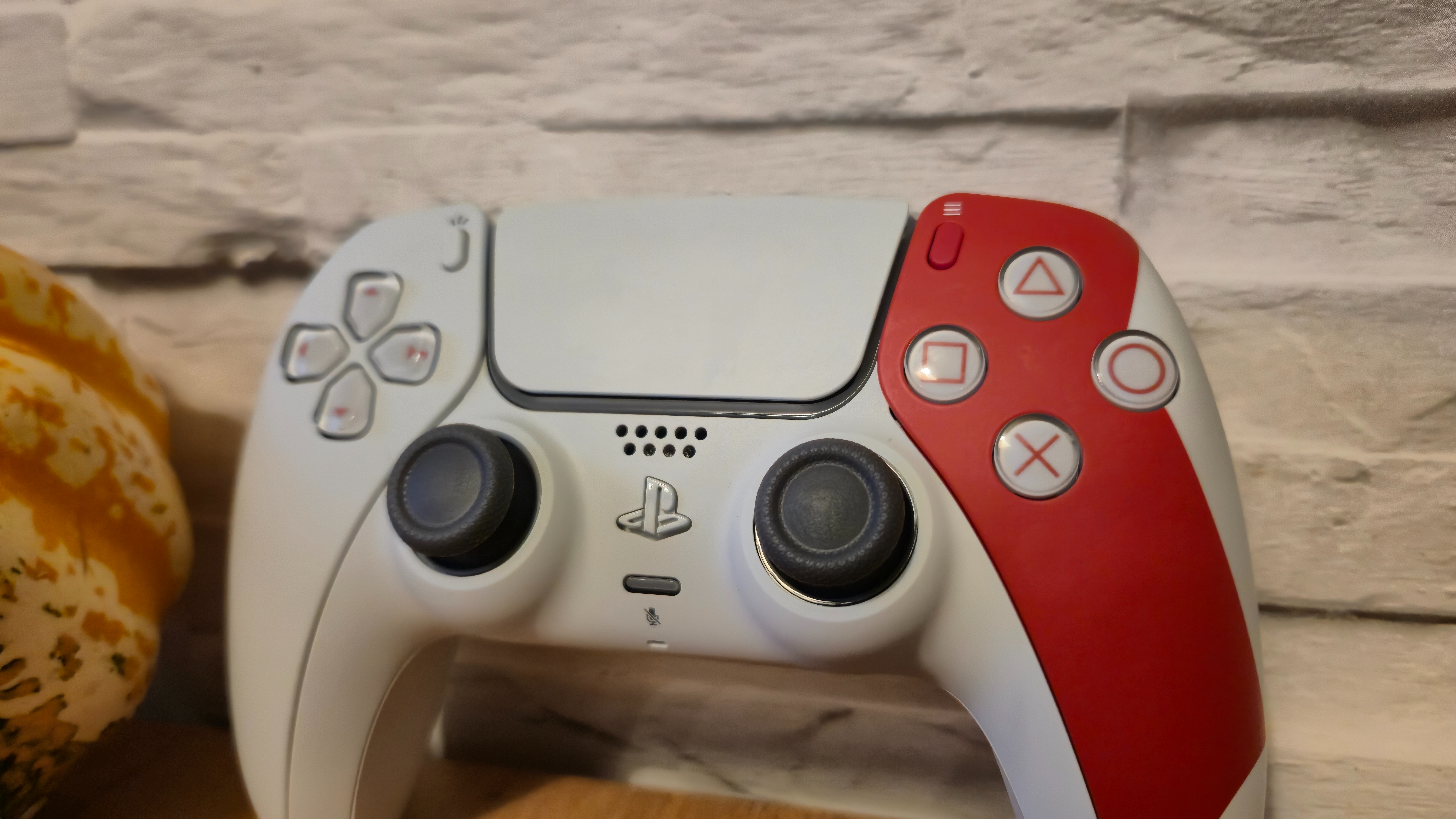 The God of War 20th Anniversary DualSense on a wooden table in front of a white brick background