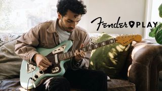 A guitarist plays a Fender guitar while seated on a couch