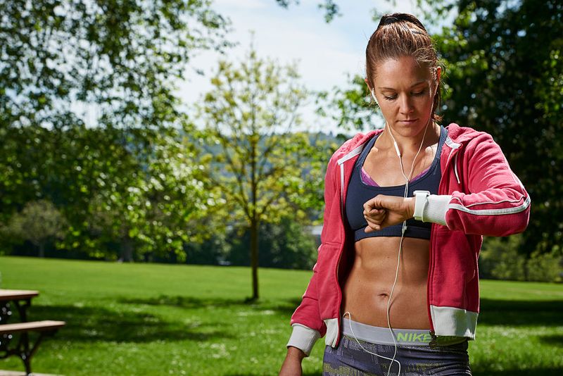 A woman in sports clothing checks her watch while out in a park