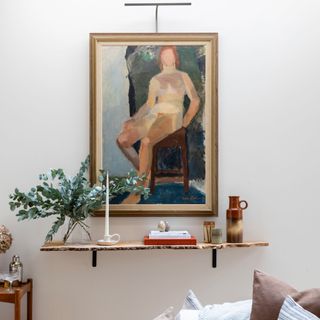 lighting over an abstract life drawing painting with minimalist bar light above and wooden shelf before with cnadle and greenery in vase