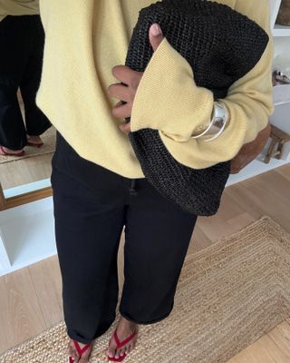 Woman wears pale yellow knit with black trousers and red sandals.