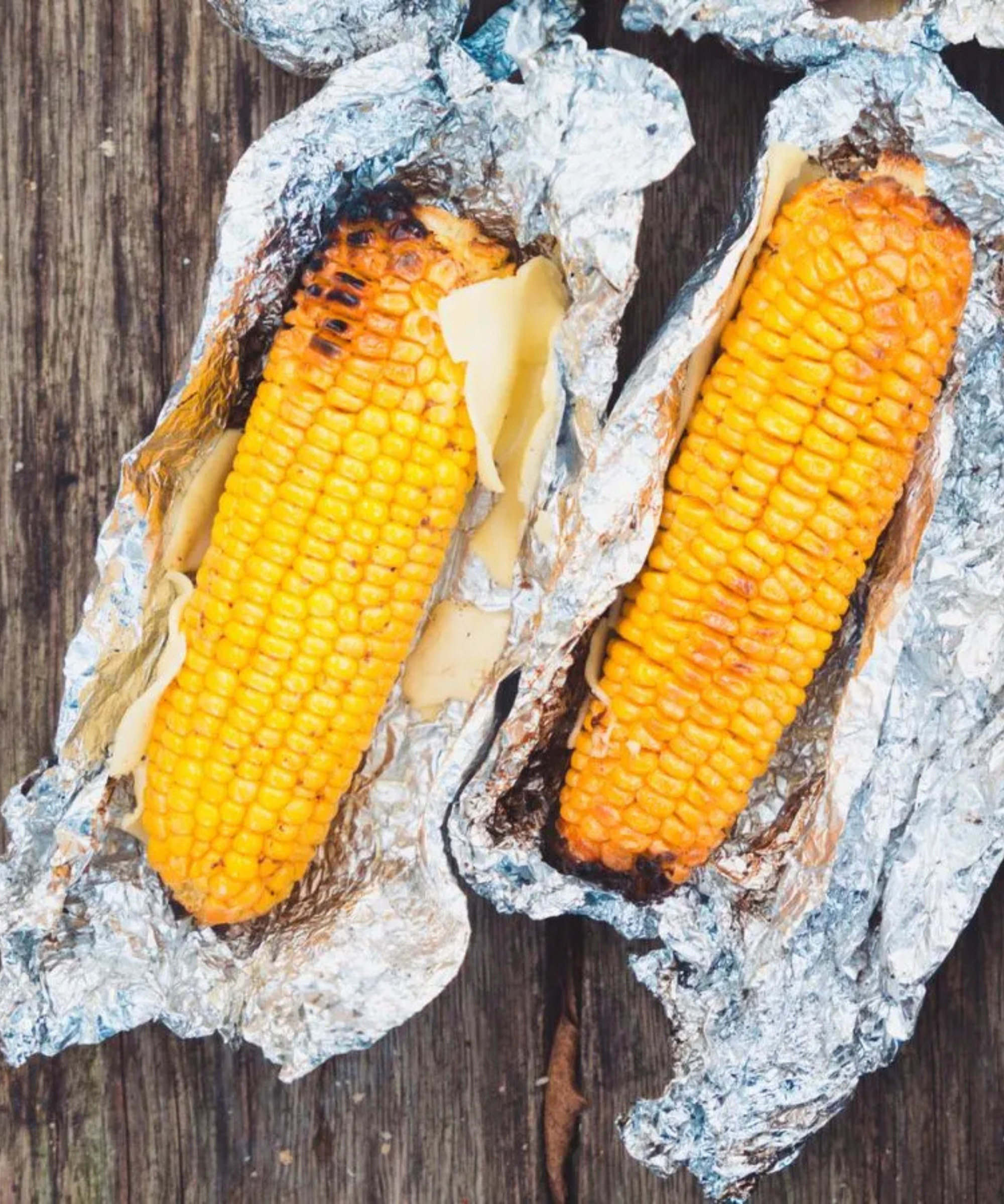 Three corn on the cobs grilled in foil with butter and cheese
