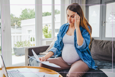 Pregnant woman holding paperwork in one hand and touching her head with the other