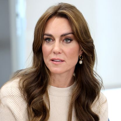 Kate Middleton has long brown hair and wears a cream sweater