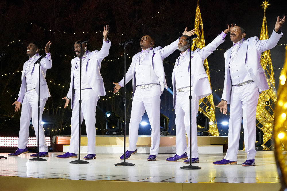 the temptations wear white suits while performing on stage in front of gold christmas trees at the 2024 motown christmas special