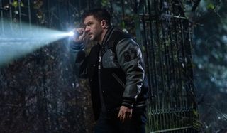 Tom Hardy investigates with a flashlight on a dark night in Venom: Let There Be Carnage.