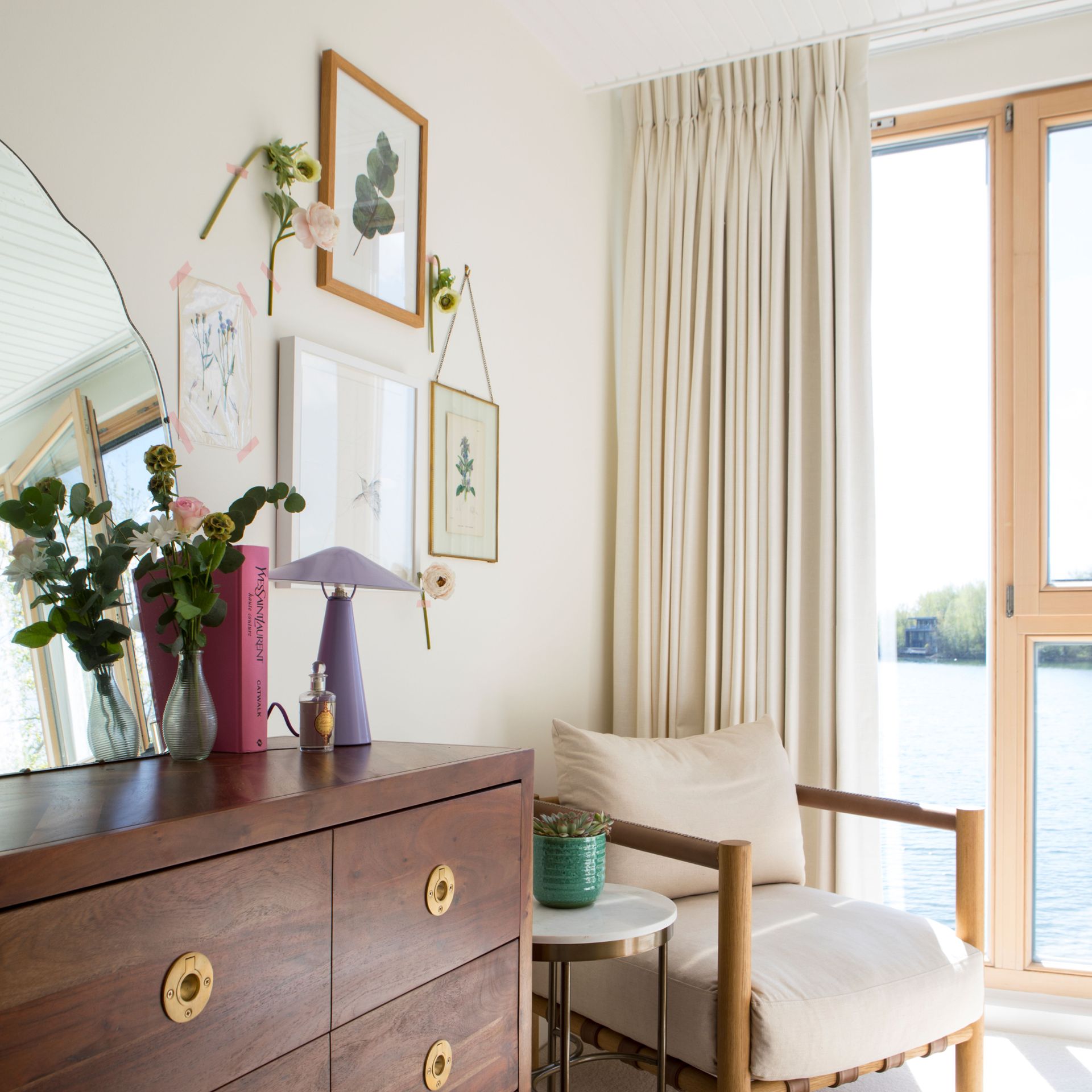 Dark wood dresser in bedroom decorated with home furnishings, armchair, next to tall windows