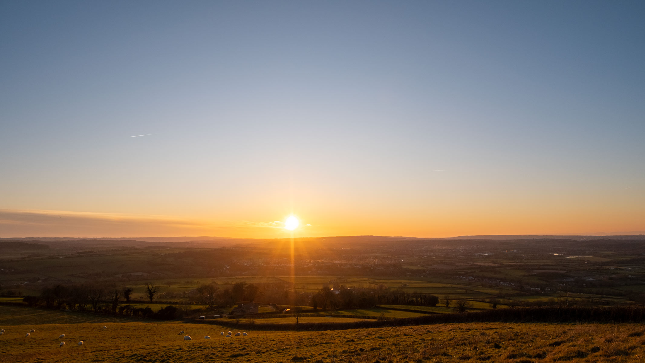 A sunset with a clear blue-and-orange sky over some fields
