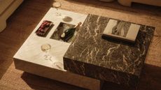a stacked marble coffee table with built-in ice bucket with a bottle of champagne, two champagne glasses and a tray of sweets on a jute rug
